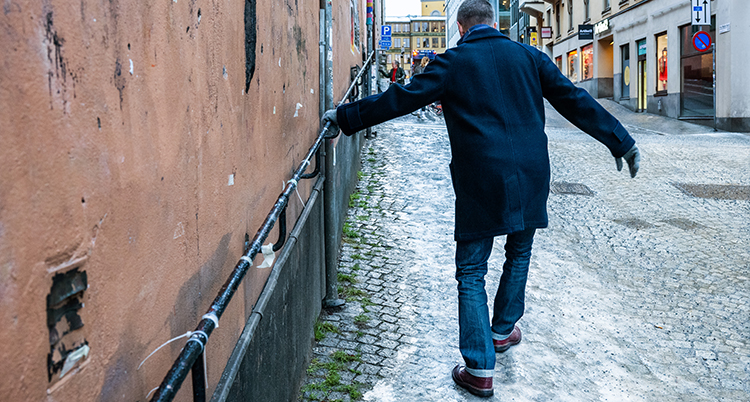 Han håller sig i en vägg. Han gåt på gatan. Gatan är isig.