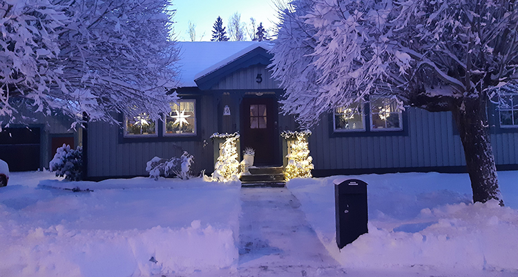 Ett hus med mycket snö runtomkring. Och dekorationer med ljus.