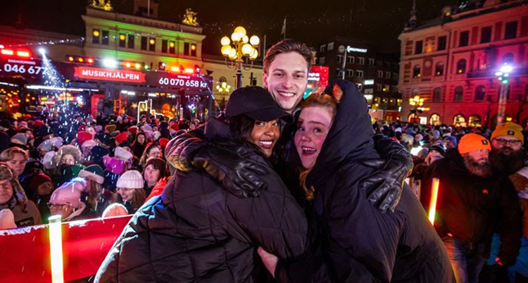 De tre programledarna kramar om varandra på torget framför massa människor.