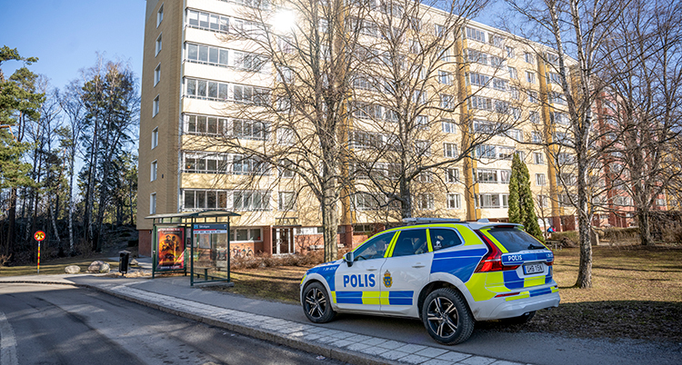 En polisbil står utanför ett hus med flera våningar.