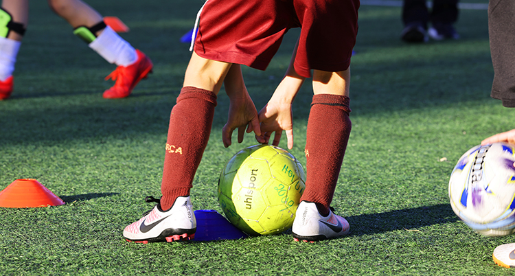 Ett barn som spelar fotboll håller fast en boll mot marken.