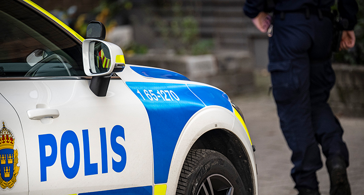 En polis står bredvid en polisbil. Hans huvud syns inte.