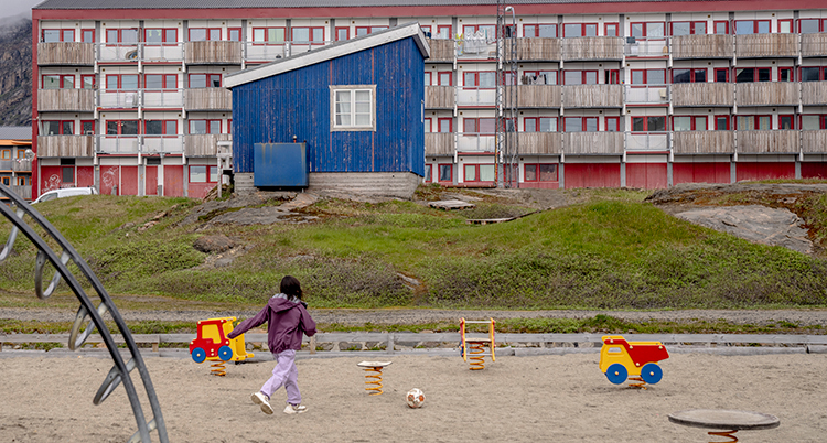 Barnet är på en lekplats framför höga hus med lägenheter.