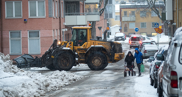 En gul traktor plogar bort snö och is på gatorna.