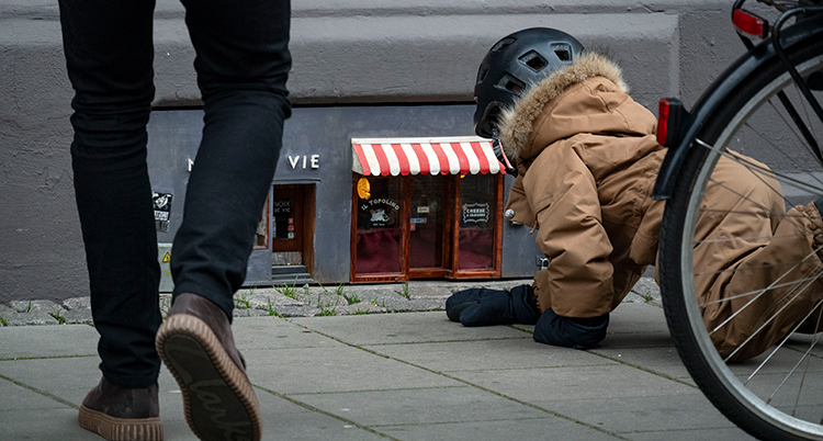 Ett barn ligger på trottoaren och tittar på den lilla affären. En vuxen går mot affären.