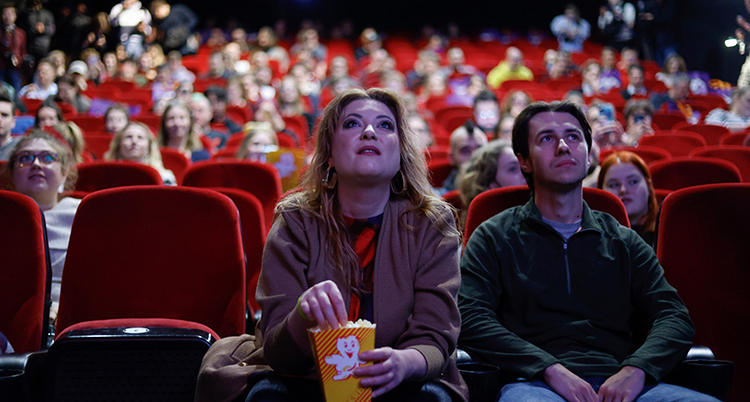 Två personer sitter framför en film på bio. De har popcorn i en låda.