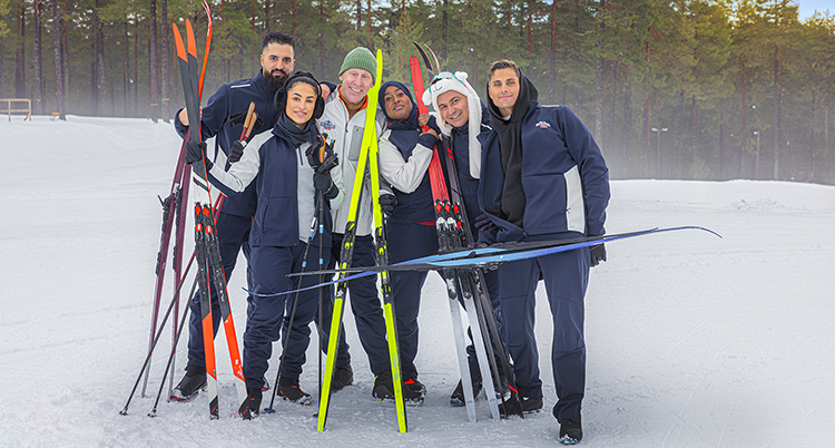 De står i en grupp ute i snön. De håller i skidor.