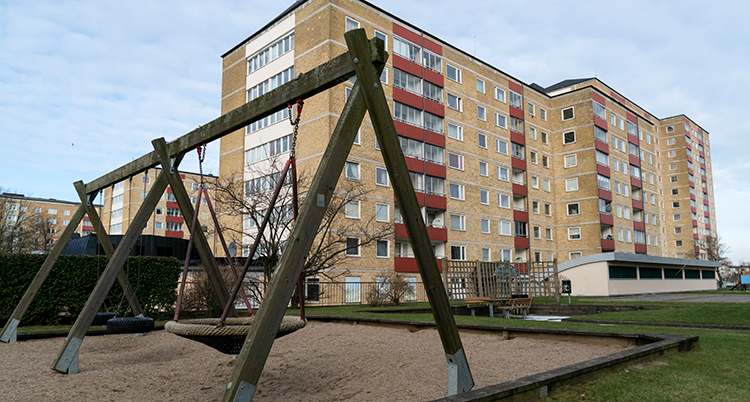 En lekplats framför ett stort hyreshus med lägenheter.