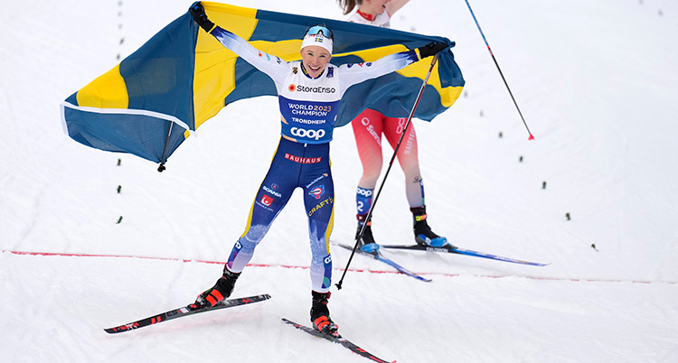 Hon åker skidor och håller i en svensk flagga.