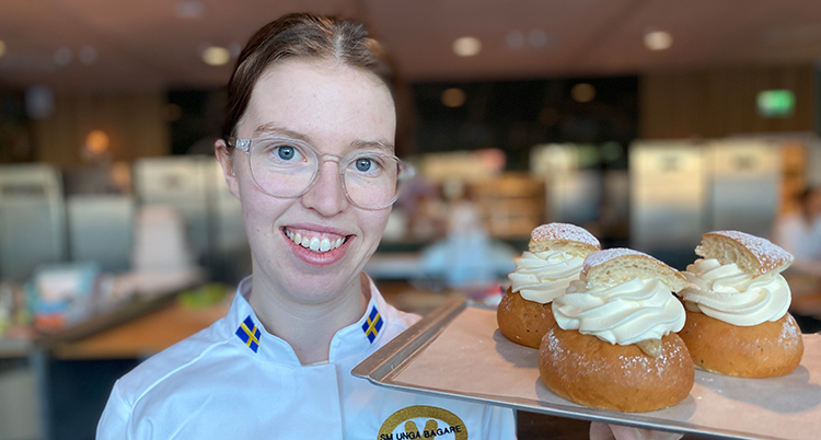 Ett porträtt. Hon har vit bagarskjorta och håller i en bricka med tre semlor.