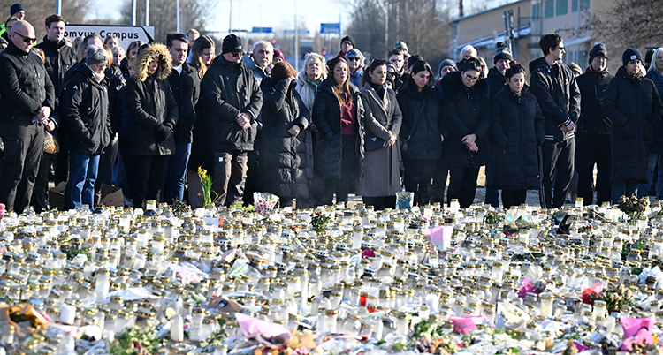 Många människor står tysta bredvid många ljus och blommor.