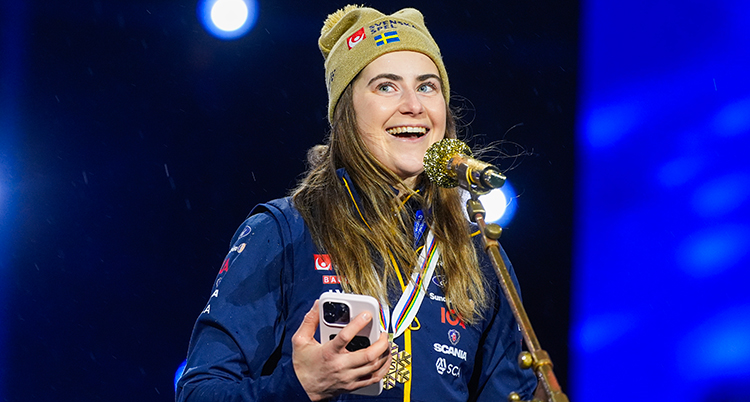 Ebba Andersson står på en scen och är glad. Hon har en medalj runt halsen.