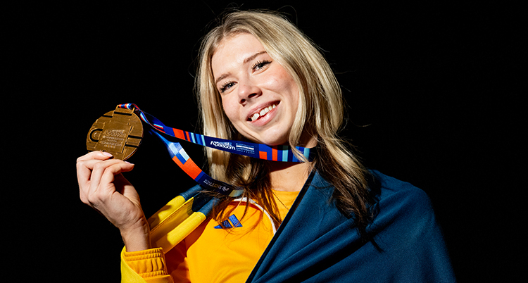 Håller upp en medalj med en flagga på sig.