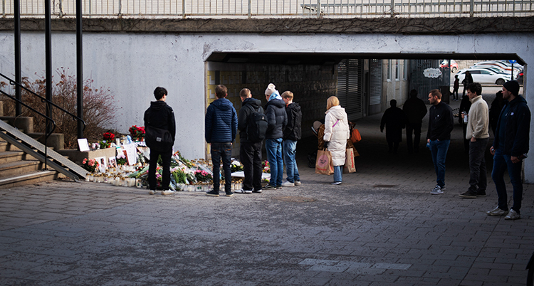 Platsen där skjutningen hände. Det står blommor och ljus där. Flera unga personer står vid platsen.