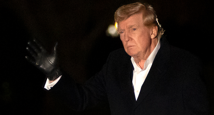 Donald Trump ser allvarlig ut och håller upp en hand. Han är utomhus och har en svart handske på handen.