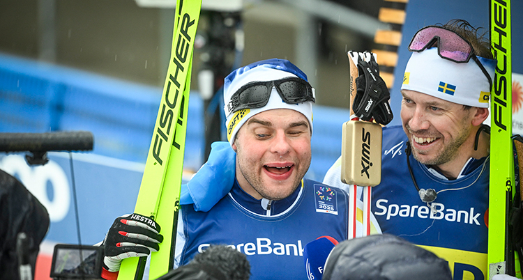 De står bredvid varandra. De håller i skidor och stavar.