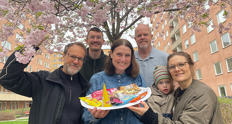 Flera personer står i en grupp och ler mot kameran. Personen i mitten håller ett fat med glassar.