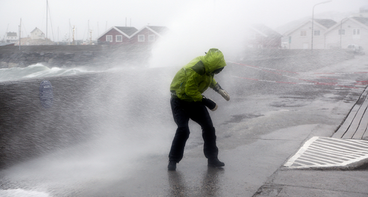 Det blåser mycket. En person står där det blåser. Han får vatten på sig från havet.