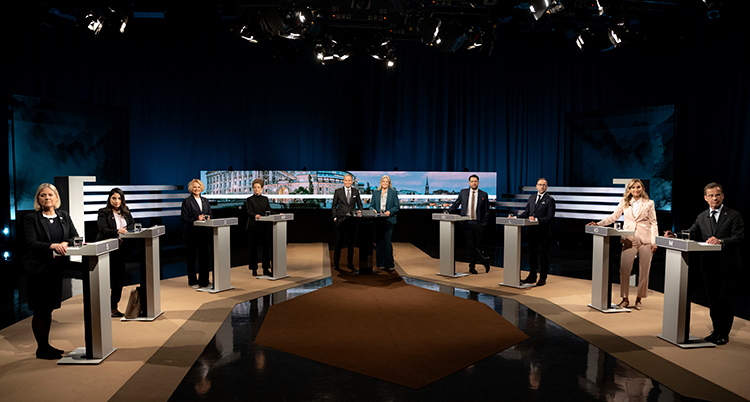 De står vid varsin talarstol i en tv-studio. I mitten står två programledare.
