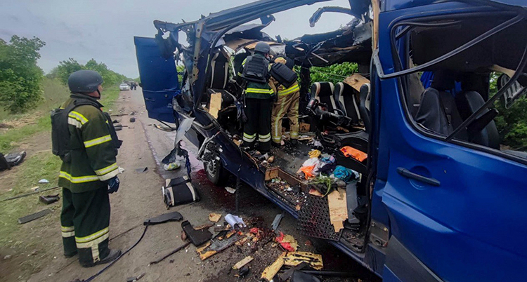 Brandmän står vid en minibuss som är helt förstörd.