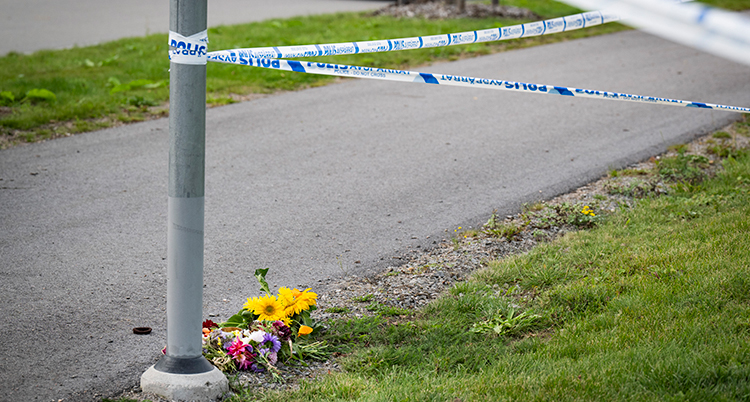 En gåbana med el lyktstolpe som det sitter polisens blå band på. Någon har lagt en liten blombukett vid stolpen.