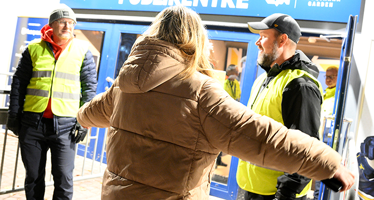 En person håller ut armarna framför två vakter med gula västar.