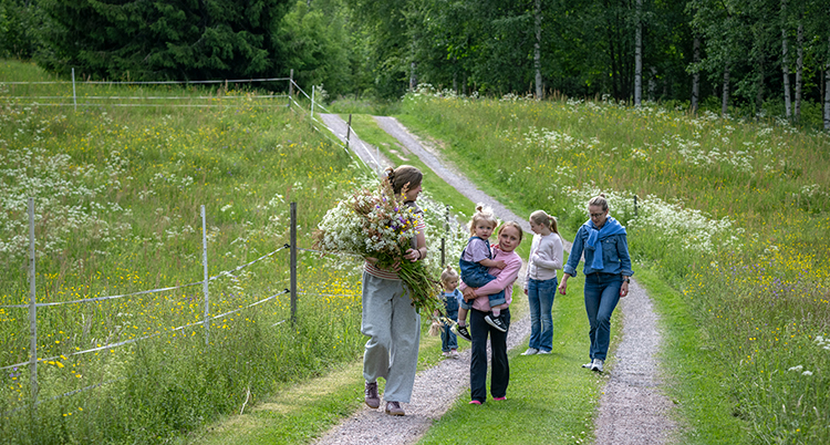 Några går på en landsväg. En av dem har en stor bukett blommor i famnen.