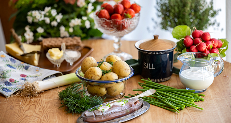 Ett bord med skålar med potatis, jordgubbar, sill, gräslök.