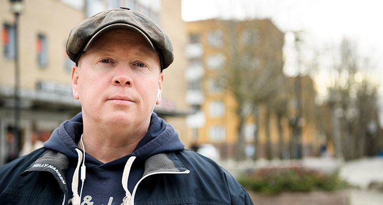 Han har en keps. Han tittar rakt in i kameran. Han står utomhus.