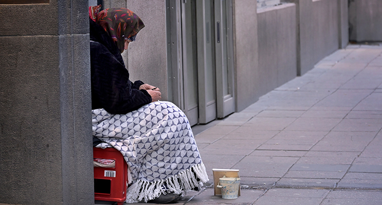 Hon sitter vig en vägg. Hon har en filt och en mugg framför sig.