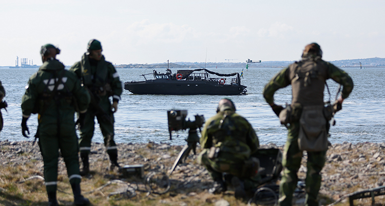 Soldater står vid en strand. Deras båt ligger en bit ut i vattnet.