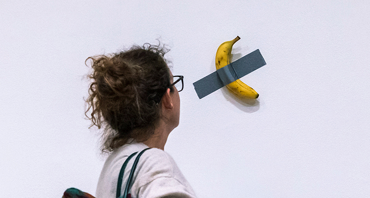 En kvinna tittar på en banan som sitter på en vit vägg. Bananen sitter fast med silvertejp.