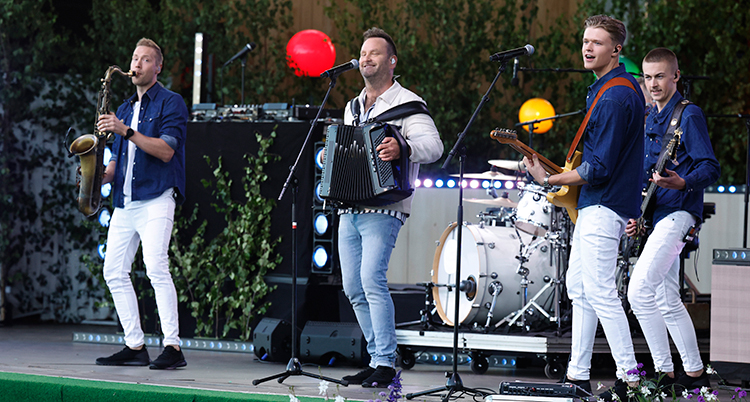 Flera glada musiker på en scen. De spelar bland annat saxofon, dragspel och gitarrer.