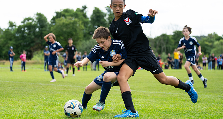 Två pojkar spelar fotboll på gräs.