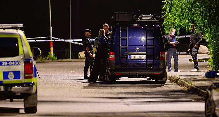 Några personer står bredvid två polisbilar. Det är natt och mörkt ute.