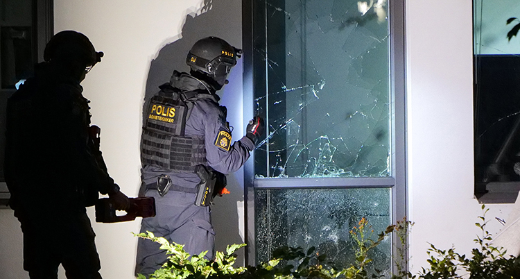Två poliser vid en trasig dörr vid ett hus.