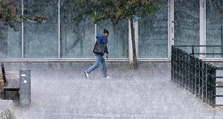 En man går i ett ösregn i en stad.