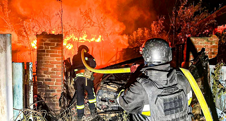 Brandmän med en slang framför en stor brand.