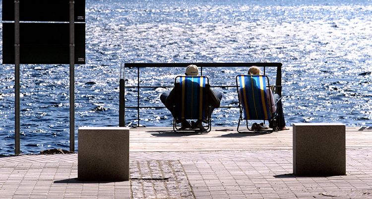 Två personer sitter i solstolar på en brygga.