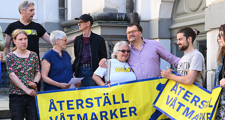 De står i en grupp. De håller i en skylt.