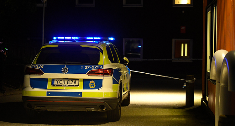 En polisbil utanför ett hus. Det är mörkt ute.