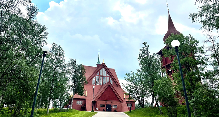 En röd kyrka i trä och ett klocktorn intill.
