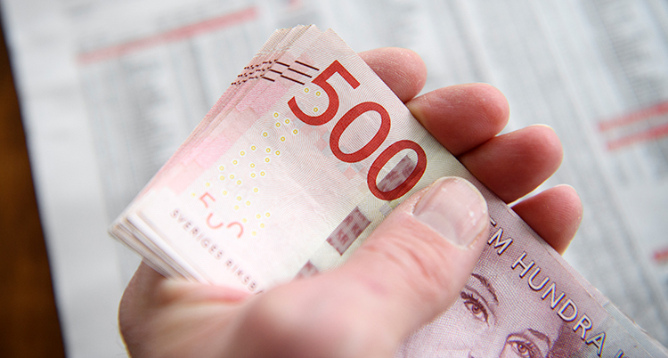 En hand som håller i sedlar som är värda 500 kronor.