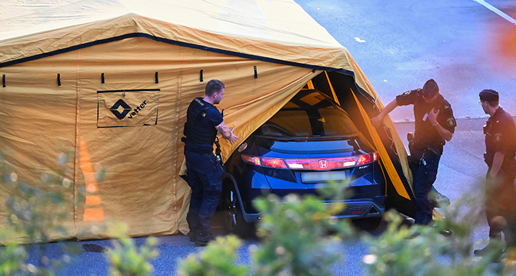 Poliser vid ett stort tält. Inne i tältet står en bil.