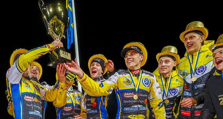 De är glada. De har guldgula hattar. En håller upp en gyllene pokal.