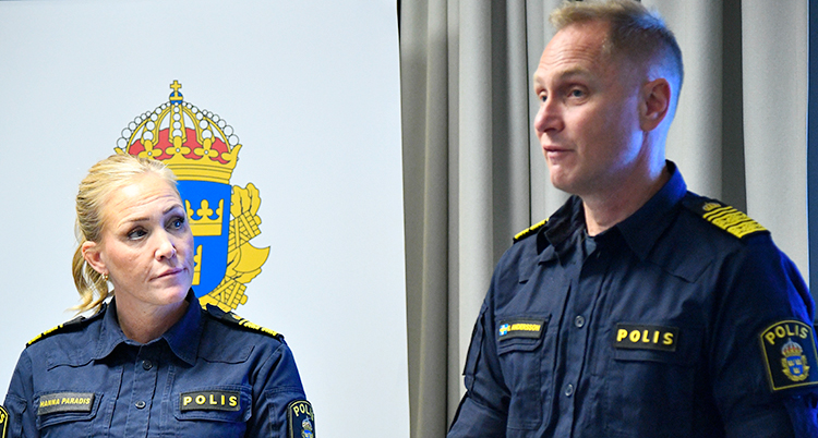 Två poliser står och pratar i mikrofoner på en träff med journalister.