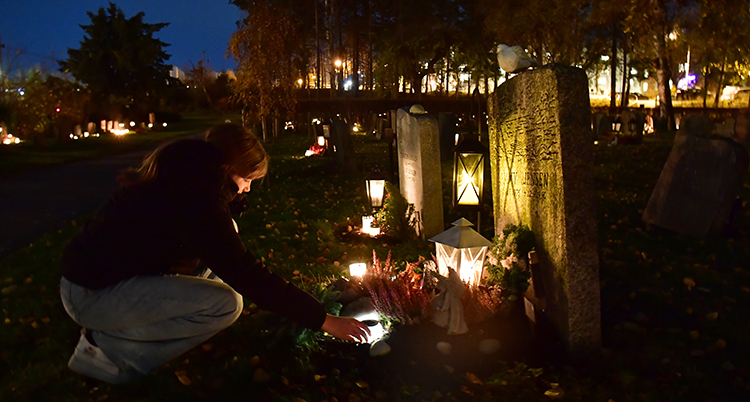 Hon sitter på huk framför en gravsten. Det lyser av ljus och lampor i mörkret.