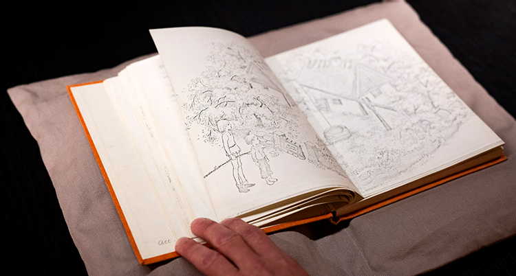 En hand bläddrar i en bok. På uppslaget syns tecknade bilder.