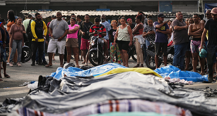 Människor står runt döda kroppar. Det är tyg över kropparna.