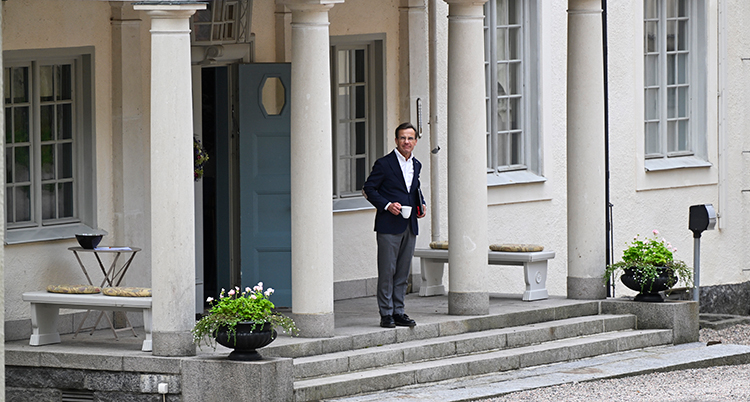 Han står på husets trappa.